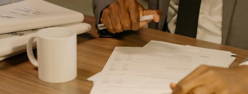 Free Close-up of a businessman holding and reviewing documents on a wooden desk. Stock Photo